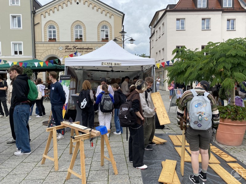 Jugendliche stehen vor einem Pavillon am Stadtplatz, probieren Werkstationen aus und beteiligen sich an einer Mitmachaktion im Rahmen eines Demokratiefestes.