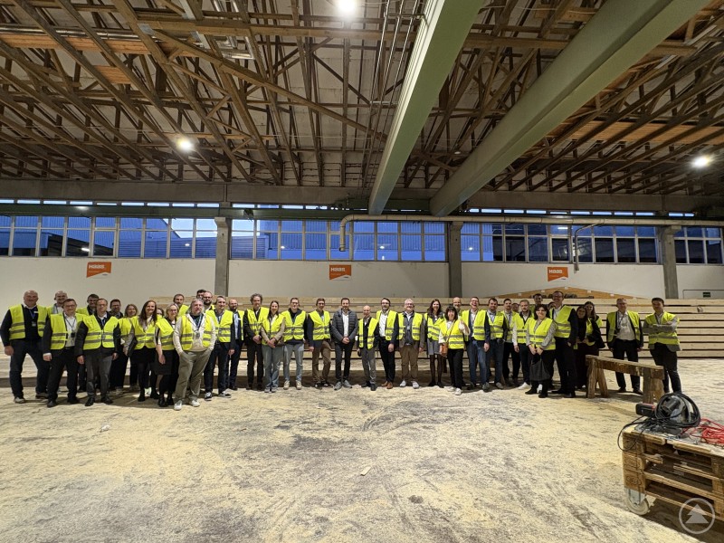 Blick hinter die Kulissen: Bei einer Werksführung erhielten die Teilnehmer vor Ort Einblicke in das serielle Bauen bei Haas Fertigbau. Große Gruppe von Teilnehmern mit Sicherheitswesten in einer Produktionshalle während einer Werksführung.