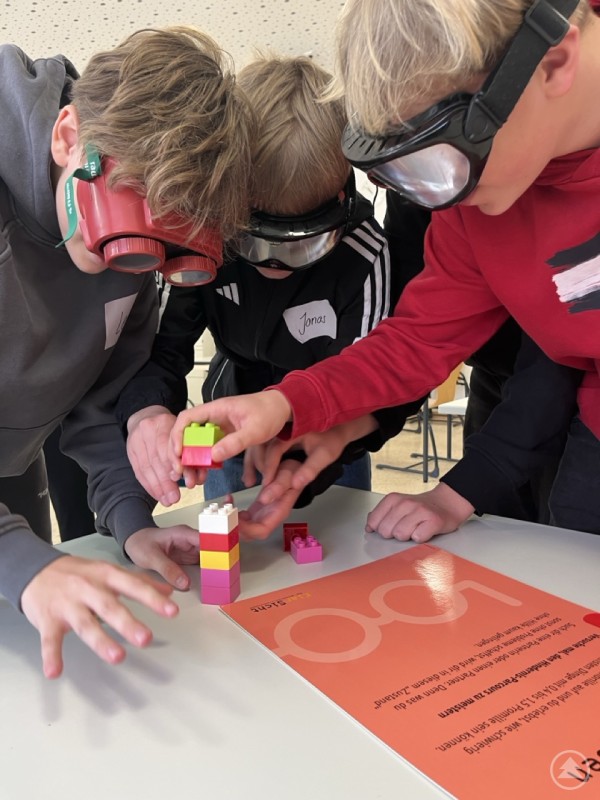 Mit Rauschbrillen wird selbst eine einfache Aufgabe zur Herausforderung Mehrere Schüler mit speziellen Brillen bauen gemeinsam mit Bausteinen, eingeschränkte Sicht erschwert die Aufgabe
