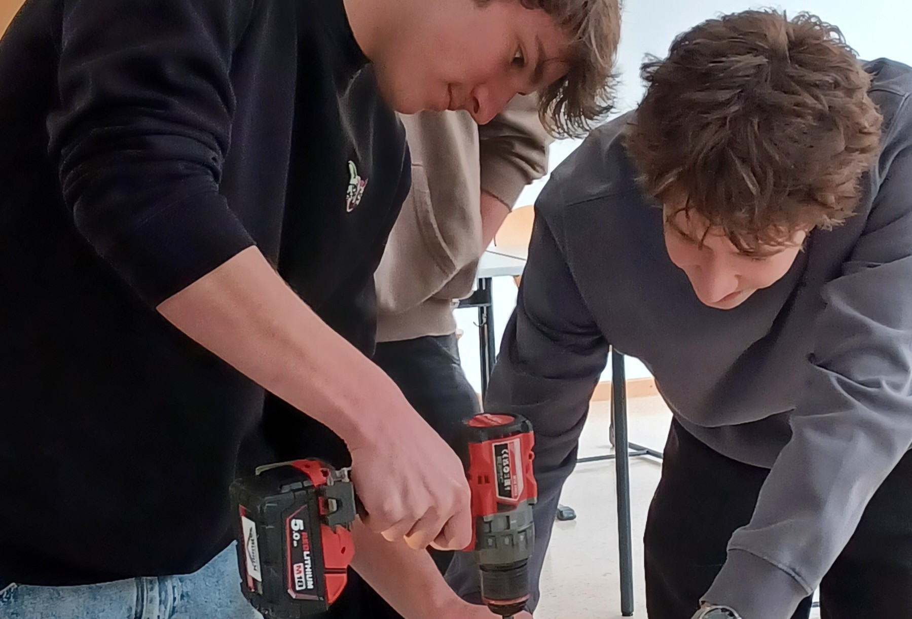 Es sind zwei Jungen zu sehen. Einer von ihnen hält eine Bohrmschine