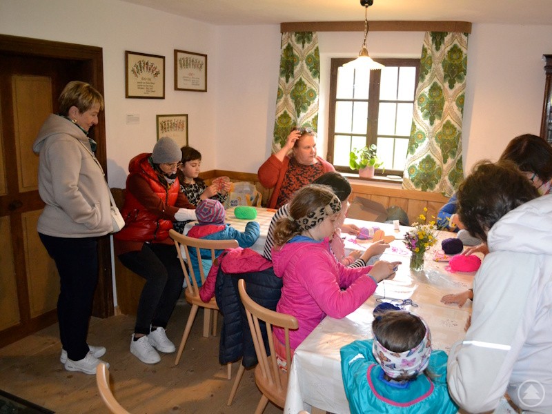 Kinder und Erwachsene sitzen gemeinsam an einem Tisch und basteln mit buntem Garn.