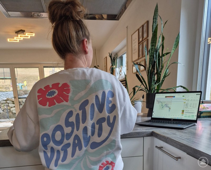 Entspannt, nebenbei - Angelika beobachtet die Kurse und wartet auf ein Einstiegssignal Angelika Sageder steht an der Küchenzeile und hat den Blick auf ihren Laptop gerichtet. Sie trägt einen Pullover mit der Aufschrift