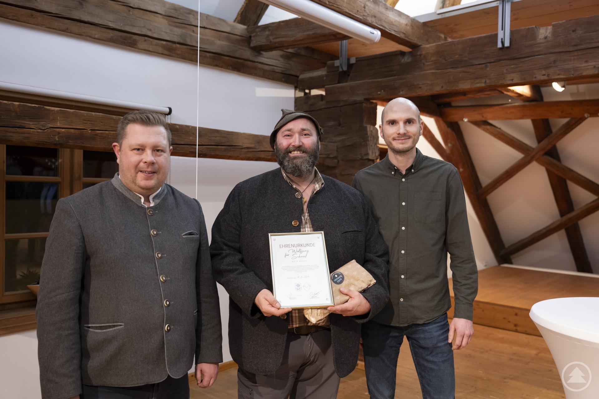 Bürgermeister Michael Adam (l.) und Tourismus-Chef Tobias Wolf (r.) bedankten sich bei Wolfgang Schreil alias „Woid Woife“ mit einer Ehrenurkunde und einem handgemachten Brotzeitbrett.