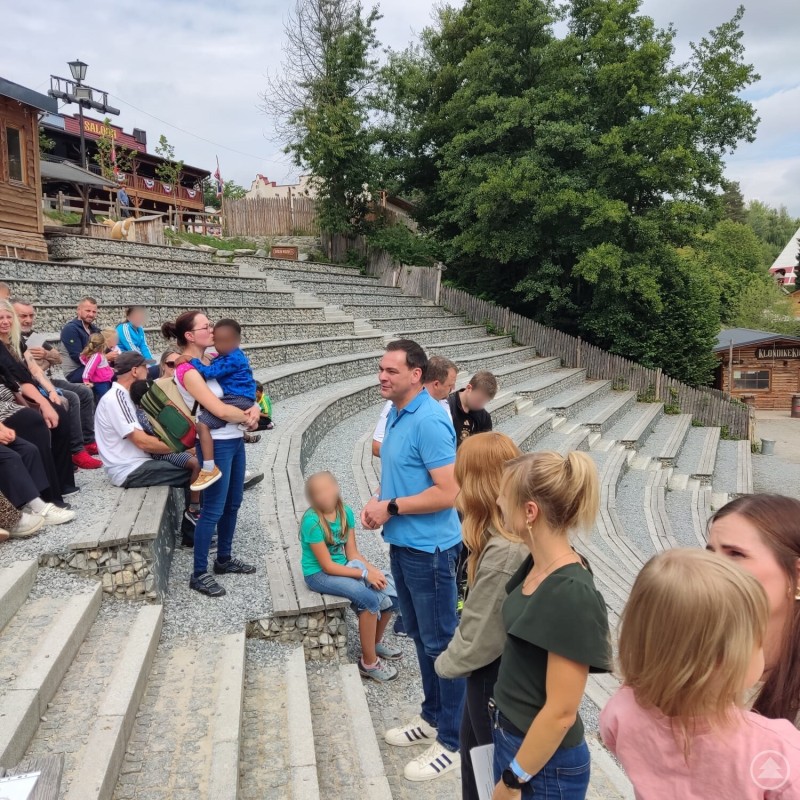Landrat Sebastian Gruber begrüßte die Pflegefamilien und dankte den Pflegeeltern für ihr Engagement. Menschen sitzen auf den Rängen eines Freilichttheaters, während ein Mann in blauem Polohemd mit Familien spricht.
