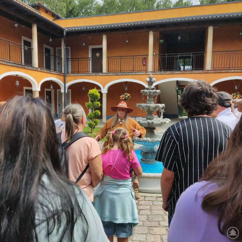 Bei der Stadtführung durch Pullman City erhielten die Pflegefamilien spannende Einblicke in den Wilden Westen. Eine Gruppe von Menschen hört in einem Hof mit Brunnen einer Person in Westernkleidung aufmerksam zu.