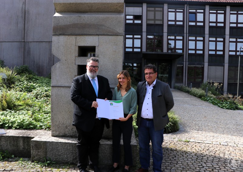 Vorstand Bernhard Hanis (von rechts) und Sophia Meixelsperger freuen sich über die Urkunde für die Teilnahme am Umwelt- und Klimapakt Bayern, die der 2. Bürgermeister Andreas Rother überreicht. Drei Personen stehen vor dem Rathaus Passau, einer hält eine Urkunde in den Händen. Es handelt sich um die Übergabe der Auszeichnung für Umweltleistungen an die BERGER Bau SE.