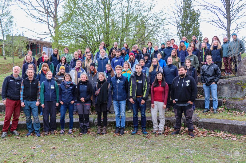 Gruppenbild der Teilnehmerinnen und Teilnehmer des 35. Commerzbank-Umweltpraktikums im Wildniscamp am Falkenstein. Große Gruppe junger Menschen mit Betreuenden im Freien, teils mit Outdoor-Kleidung, vor Bäumen versammelt.