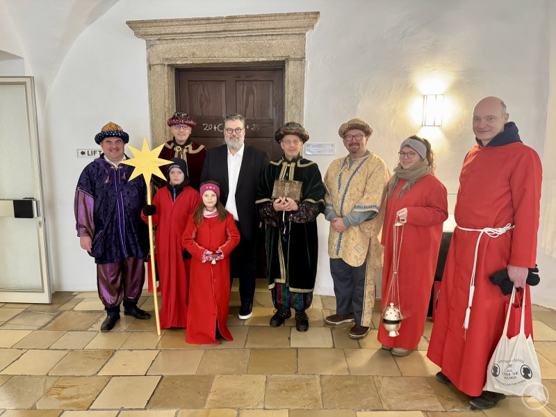 Bürgermeister Andreas Rother (3. v. l.) empfing Markus Biber (von links), Konrad Mader, Dr. Roland Feucht und Alexander Köllnberger als Heilige Drei Könige sowie die Ministranten im Rathaus. Eine Gruppe von neun Personen, darunter Erwachsene und Kinder, ist als Sternsinger und Ministranten verkleidet. Sie tragen farbenfrohe Gewänder, einige halten einen Stern oder eine Räucherfass, in der Mitte steht Bürgermeister Andreas Rother im dunklen Anzug. Die Gruppe steht in einem hellen Flur mit Steinboden und blickt in die Kamera.