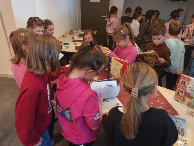 Die Schülerinnen und Schüler der Grundschule Spiegelau entdecken begeistert die neuen Bücher. Eine Gruppe von Grundschulkindern in bunten Pullovern stöbert neugierig an den Tischen mit Kinderbüchern und liest in den ausgestellten Büchern.