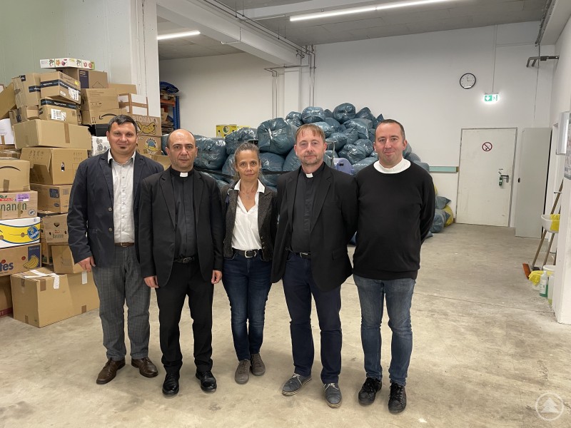 Aus Satu Mare nach Passau: Das Team der Caritas Rumänien nahm den weiten Weg auf sich. Fünf Personen, darunter zwei Geistliche, stehen in einem Lagerraum vor Kartons und Kleidersäcken und posieren gemeinsam für ein Foto.