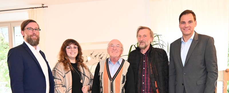 Landrat Sebastian Gruber (rechts), Sachgebietsleiter Christian Fiebig und Kulturreferentin Gabriela Rauscher (von links) dankten den beiden Archivpflegern Hermann Kurz (Mitte) und Richard Schiffler für ihre jahrzehntelange, ehrenamtliche Arbeit. Fünf Personen stehen lächelnd nebeneinander in einem hellen Raum. In der Mitte befinden sich zwei ältere Männer, flankiert von drei Personen aus Verwaltung und Kultur. Die Gruppe blickt freundlich in die Kamera.