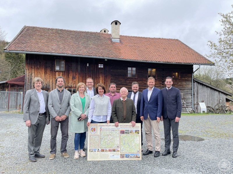 Die Bürgermeister der Gemeinden auf böhmischer und bayerischer Seite, gemeinsam mit Projektverantwortlichen Veronika Koci und Heinrich Vierlinger sowie Bezirkstagspräsident Dr. Olaf Heinrich und Landrat Sebastian Gruber, feiern den Start des Projekts „Lamberg-Pfad“. Gruppenfoto der Bürgermeister und Projektverantwortlichen vor einem traditionellen Holzgebäude in Finsterau anlässlich der Vorstellung des Lamberg-Pfads.
