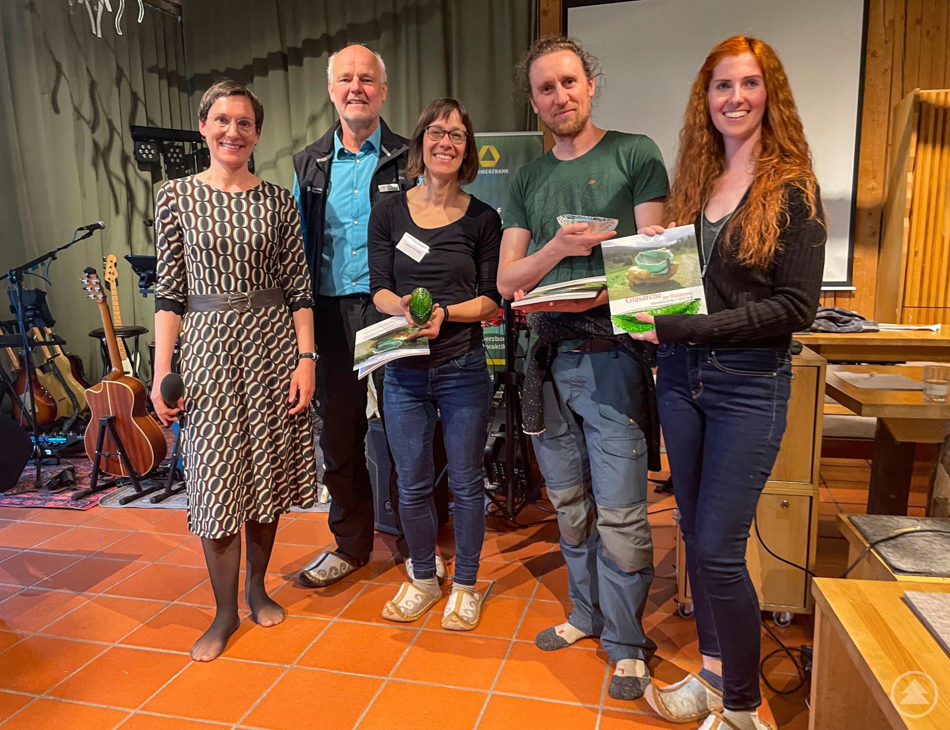 Nationalparkleiterin Ursula Schuster, Andrea Hoffmann (NNL), Stiftungskurator Sinan von Stietencron und Katrin Moser (Commerzbank) verabschiedeten Lukas Laux. Fünf Personen bei einer Abschiedsveranstaltung, eine Frau hält ein Buch, eine andere ein Mikrofon.