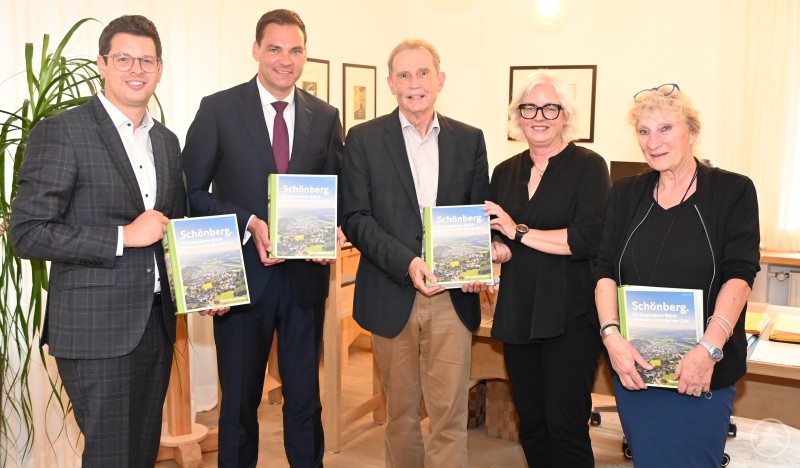 In Begleitung von Bürgermeister Martin Pichler (l.) überreichten Hannelore Hopfer (v.r.), Edith Döringer und Bernd Bachhuber das Landratsexemplar, das zu Gemeingut der Kreisbibliothek werden soll, an Landrat Sebastian Gruber, der sich dafür ganz herzlich bedankte. Fünf Personen stehen nebeneinander in einem Büro, alle halten ein Exemplar der neuen Schönberger Heimatchronik in den Händen und lächeln in die Kamera.