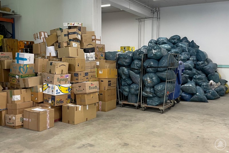 Ein Lagerraum voller gestapelter Kartons und großer blauer Kleidersäcke, die sortiert und transportbereit sind.