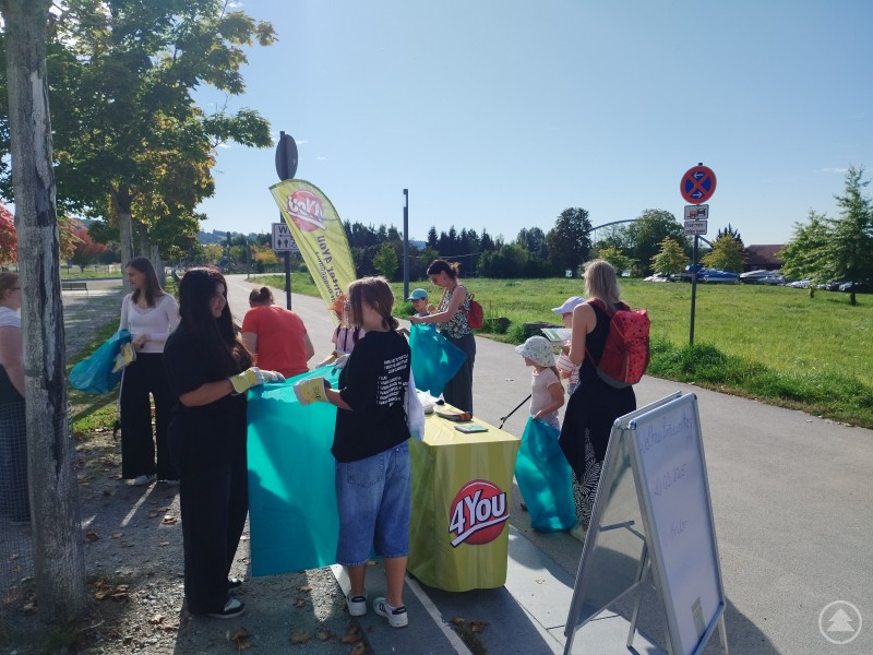 Teilnehmende des Weltaufräumtags holen sich am Stand des Jugendcenters 4You Müllsäcke und Handschuhe ab. Kinder und Erwachsene bereiten sich gemeinsam auf die Sammelaktion vor.