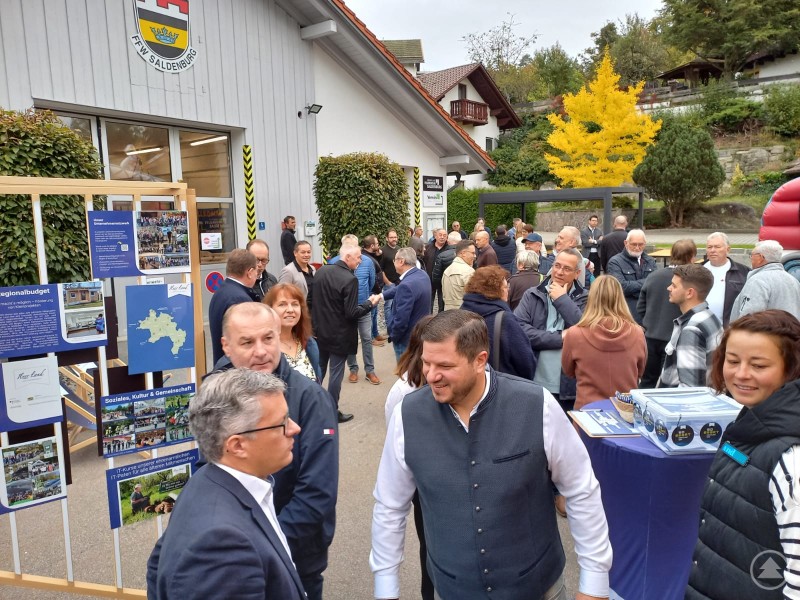 Tourabschluss in Saldenburg zur Eröffnung des Hybriden Dorfzentrums „Verein(t)“. Menschenmenge vor der Feuerwehr Saldenburg beim Tourabschluss der Jubiläumstour. Besucher informieren sich an Infotafeln, im Hintergrund ist das neue Dorfzentrum zu sehen.