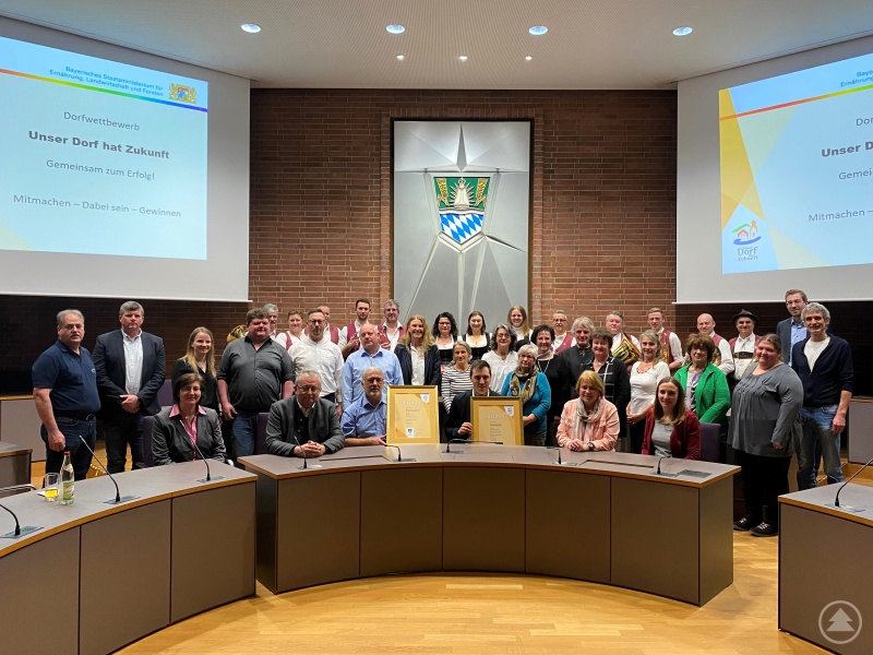 Foto: Die beiden Bürgermeister Thomas Schuster und Dr. Simon Haas (mitte sitzend mit den Urkunden) gemeinsam mit Landrat Josef Laumer, der Kreiskommission und den Abordnungen der beiden Gemeinden bei der Auszeichnung im Landratsamt.