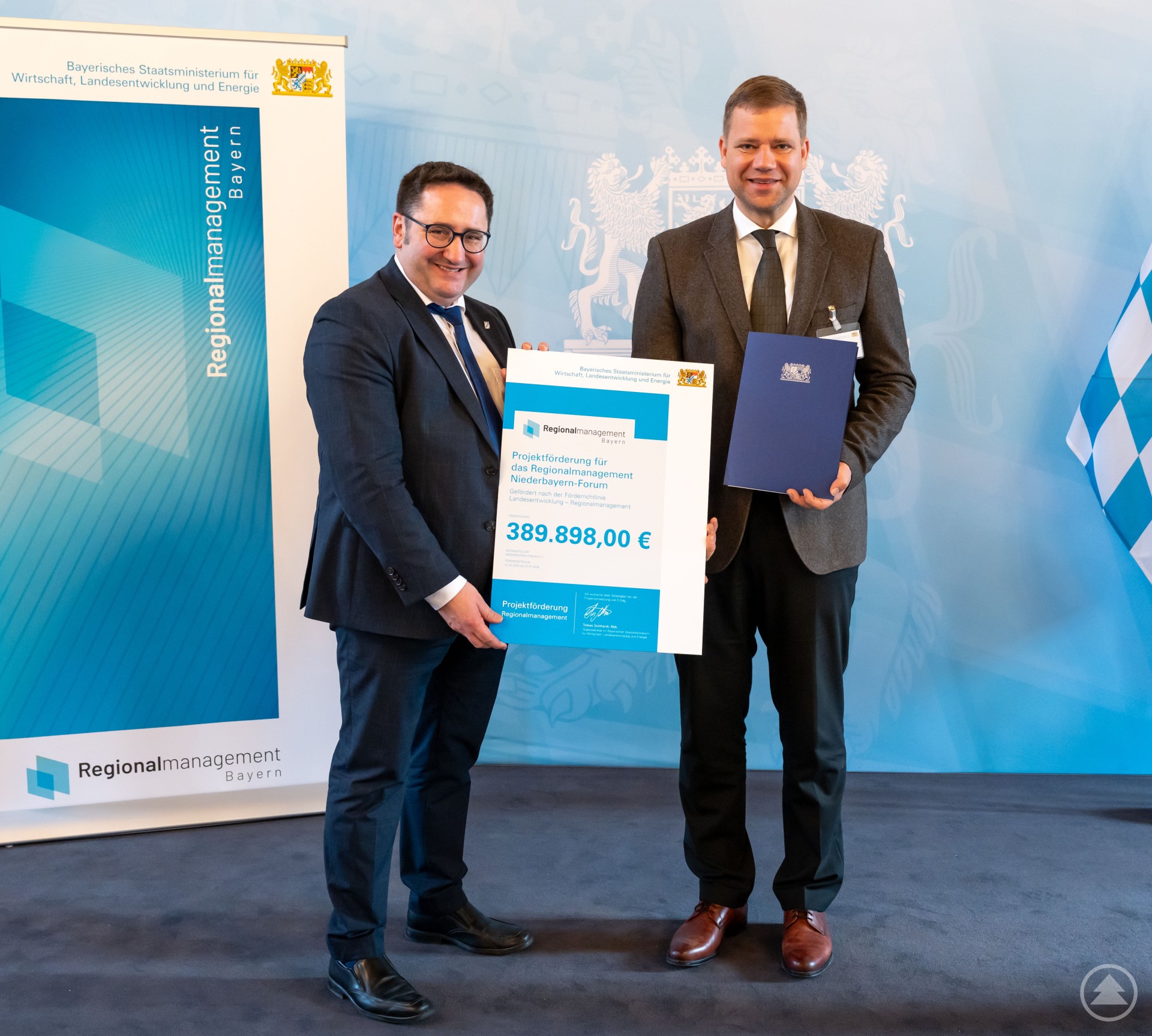 Staatsekretär Tobias Gotthardt (links) übergab Dr. Olaf Heinrich, Bezirkstagspräsident und Vorsitzender des Niederbayern-Forums, den Förderbescheid.