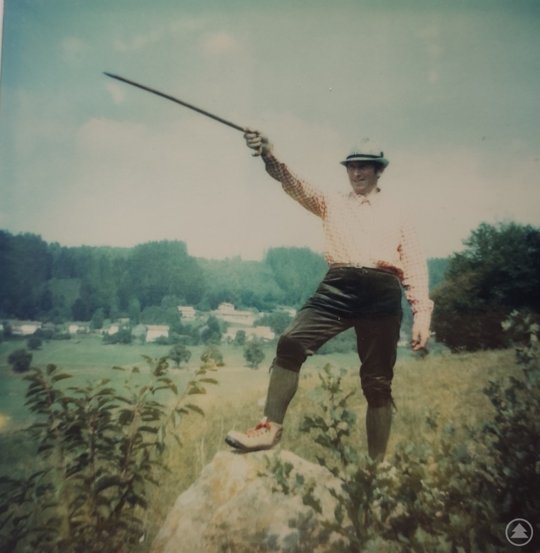Eines der eher selteneren Fotos mit Josef Peter zeigt ihn mit „Richtungsangabe“: Do geh´ i hi! Ein Mann steht in traditioneller Kleidung mit einem Wanderstock auf einem Felsen und deutet mit ausgestrecktem Arm in die Ferne.