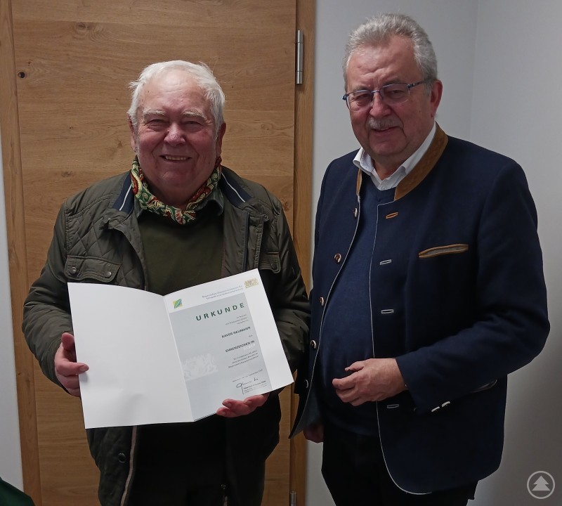 Biberberater Xaver Neumeier (links) erhält von Landrat Josef Laumer die Urkunde für mindestens 20-jährige Tätigkeit. Zwei Männer stehen in einem Innenraum vor einer Holztür. Links hält ein älterer Mann eine geöffnete Urkunde, rechts steht Landrat Josef Laumer daneben.
