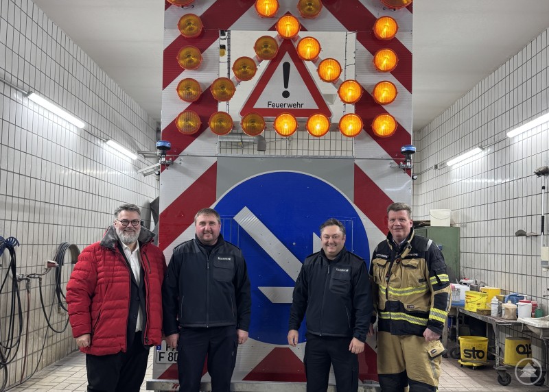 Bürgermeister Andreas Rother (li.) übergibt den neuen Verkehrssicherungsanhänger an (v. l.) den stellv. Kommandanten Josef Winklhofer und Kommandanten Martin Sagmeister im Beisein von Stadtbrandrat Andreas Dittlmann (re.). Vier Männer stehen in einer Fahrzeughalle vor einem Verkehrssicherungsanhänger mit großen Warnleuchten und einem Feuerwehr-Warnschild.