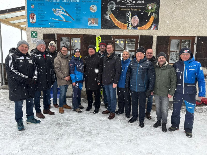 Otto Baumann, Walter Knoller, Florian Wimmer, Bürgermeisterkandidat Johannes Ramesberger, Margit Uhrmann, StM Christian Bernreiter, Florian Höpfl, MdL Josef Heisl, Adolf Kosak, Altlandrat Franz Meyer, Manfred Miggisch, Bezirksrat Stephan Gawlik, Andreas Schmid. Mehrere Vertreter aus Politik und Sport stehen bei Schneefall vor dem Vereinsheim des WSV-DJK Rastbüchl und posieren gemeinsam für ein Gruppenfoto.