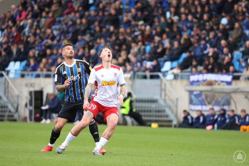 Zwei Spieler sprinten nebeneinander &uuml;ber das Spielfeld und beobachten den Ball &uuml;ber ihnen.