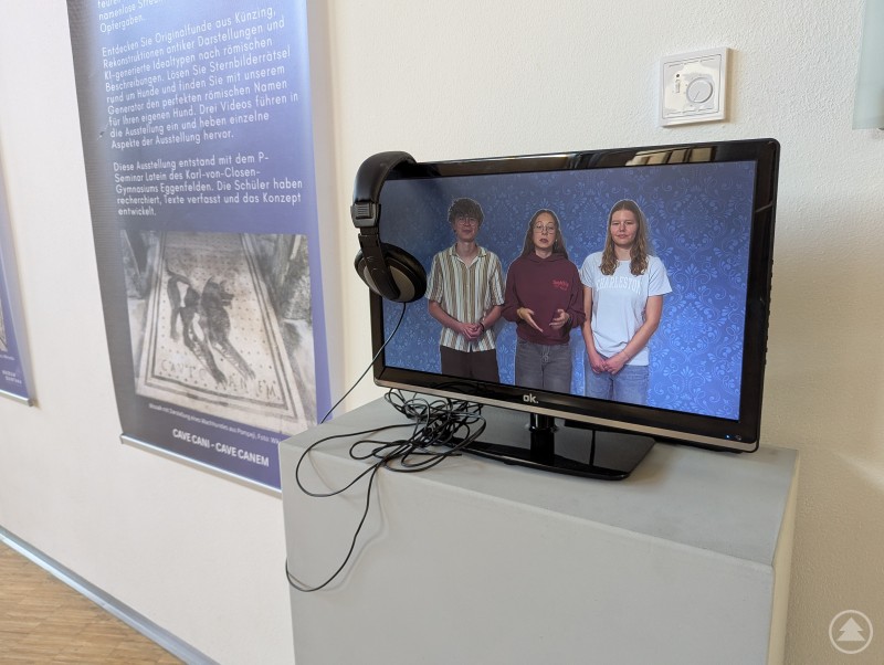 Flachbild-Fernseher zeigt ein Video mit drei Jugendlichen, die Ausstellungsinhalte erklären