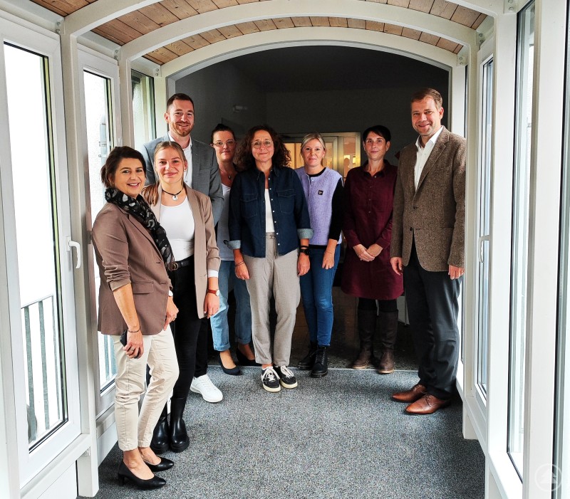 Tauschten sich über aktuelle Herausforderungen und Entwicklungen in der Suchthilfe aus: (v. li. n. re.) Alexandra Aulinger-Lorenz, Lisa-Marie Liebl, Florian Kasparak, Karin Saller, Heidi Haidn, Christiane Sterr, Verena Greiner und Dr. Olaf Heinrich. Acht Personen stehen gemeinsam in einem hellen Flur mit Glasfronten. Sie blicken lächelnd in die Kamera. Es handelt sich um Vertreterinnen und Vertreter des Caritasverbands Freyung-Grafenau sowie Bezirkstagspräsident Dr. Olaf Heinrich, die sich über aktuelle Entwicklungen in der Suchthilfe austauschten.