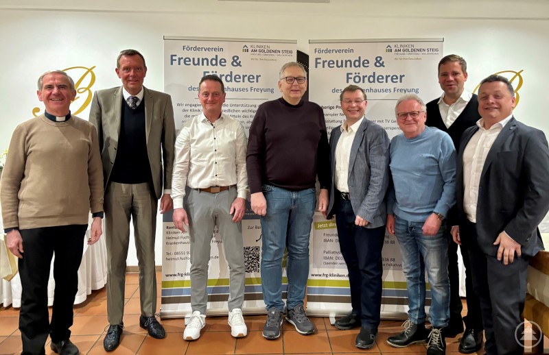 Dekan Magnus König, Geschäftsführer Marcus Plaschke, Schriftführer Helmut Fuchs, Ärztlicher Direktor Dr. Motzek-Noé, Stadtrat Sebastian Schultz, Kassenprüfer Peter Sammer, Bürgermeister Olaf Heinrich, Schatzmeister Daniel Reitmayr. Acht Männer stehen nebeneinander in einem festlich eingerichteten Raum vor zwei Roll-Up-Bannern des Fördervereins „Freunde & Förderer des Krankenhauses Freyung“. Die Gruppe lächelt und wirkt freundlich und engagiert. Im Hintergrund ist das Logo des Landhotels zu sehen.