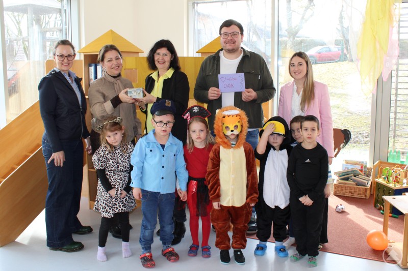 von links: Sabine Bauernfeind Ausbildung und Qualifizierung Agentur für Arbeit Passau, Ursula Rüther Regionalleitung Stadt Passau, Eva-Maria Kelch Leiterin Agentur für Arbeit Passau, Dominik Wiesmann Leiter Kindergarten, Laura Fuller stv. Kindergartenleitung, mit den Kindergartenkindern Mehrere Erwachsene stehen gemeinsam mit verkleideten Kindergartenkindern in einem hellen Gruppenraum. Ein Mann hält eine Karte mit der Aufschrift Herzlichen Dank, die Kinder tragen unter anderem Kostüme als Löwe, Polizist und Leopard.