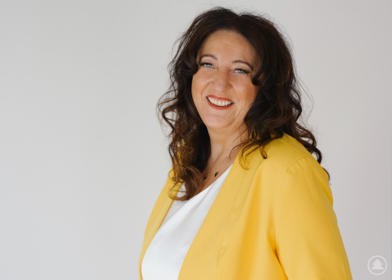 Vielseitige Arbeitstage machen Jeanette Maier aus Jeanette Maier mit gelben Oberteil vor beigen Hintergrund.