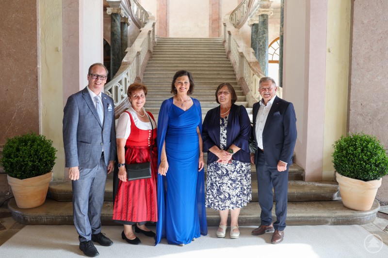 Ein persönlicher Höhepunkt des Sommerempfangs war die Begegnung mit Landtagspräsidentin Ilse Aigner. Eine Gruppe von fünf Personen posiert im Foyer von Schloss Schleißheim vor einer eindrucksvollen Freitreppe. In der Mitte steht Ilse Aigner in einem königsblauen Kleid.