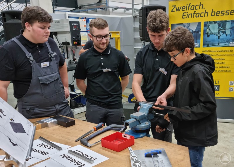 Jugendliche probieren sich an einer Werkbank mit Schraubstock und Werkzeugen aus. Jugendliche und Auszubildende arbeiten gemeinsam an einem Schraubstock und zeigen handwerkliche Techniken.