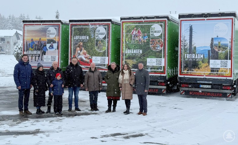 Beim Fototermin zur Präsentation der neu gestalteten LKW-Auflieger am vergangenen Wochenende zeigten sich die Beteiligten bei winterlichen Bedingungen sehr angetan von den neuen Werbe-LKWs (von links): Landrat Sebastian Gruber, Juniorchefin Kathrin Brunnhölzl, Firmeninhaber Rudolf Brunnhölzl und Enkel Max sowie die Tourismusverantwortlichen Andreas Gründinger (Waldkirchen), Robert Kürzinger (Ferienregion Nationalpark Bayerischer Wald), Monika Mittermeier (Ilztal & Dreiburgenland), Landkreis-Tourismusreferentin Johanna Anetzberger und Hohenaus Bürgermeister Josef Gais. Eine Gruppe von zehn Personen steht im Schnee vor vier LKW-Aufliegern, die jeweils mit großflächigen, farbenfrohen Werbemotiven für den Bayerischen Wald beklebt sind. Die winterliche Szene zeigt im Hintergrund schneebedeckte Bäume und Häuser, während auf den LKWs touristische Slogans und Bilder zu sehen sind.