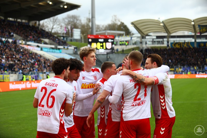 Mehrere Spieler des SSV Jahn Regensburg stehen eng zusammen und feiern gemeinsam auf dem Spielfeld.