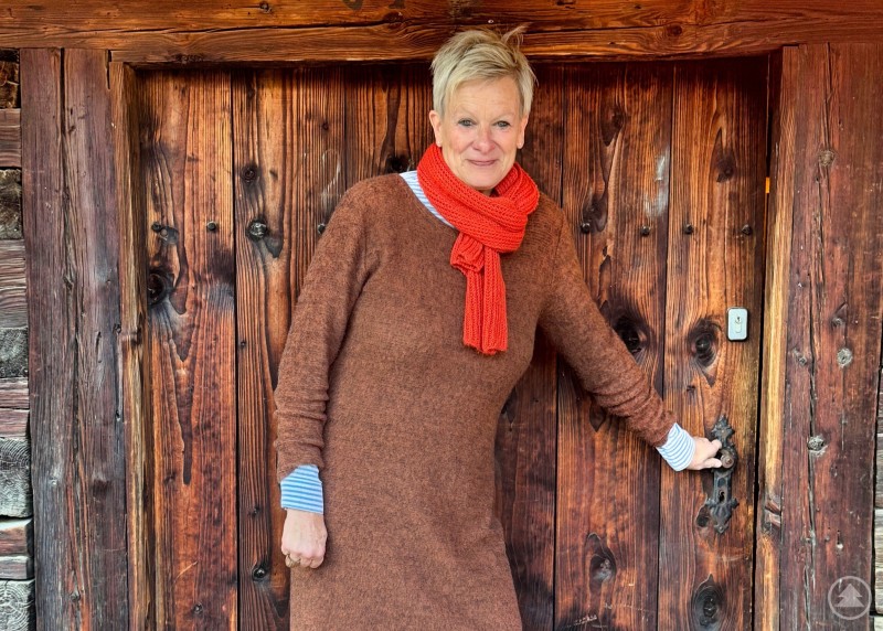 Betriebsleiterin Silke Holzner schließt die Tür des Schusteröderhofes im Massinger Freilichtmuseum bis zum Saisonstart im nächsten Frühling. Eine Frau steht vor einer alten, rustikalen Holztür. Sie trägt ein braunes Strickkleid, graue Leggings, braune Stiefel und einen roten Schal. Die Szene wirkt herbstlich und warm.