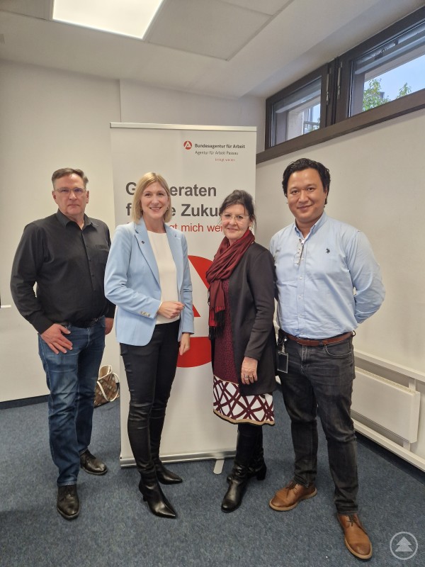 Bildunterschrift von links: Torsten Langguth (Teamleiter Arbeitsvermittlung), Martina Hamedinger (Vice President Human Resources FACC), Eva-Maria Kelch (Leiterin Arbeitsagentur Passau) und Tim Nguyen (Recruiter FACC) Vier Personen stehen vor einem Roll-up der Agentur für Arbeit Passau in einem Büro. Zwei Frauen und zwei Männer posieren nebeneinander und lächeln freundlich in die Kamera. Im Hintergrund ist das Logo der Agentur für Arbeit sichtbar.