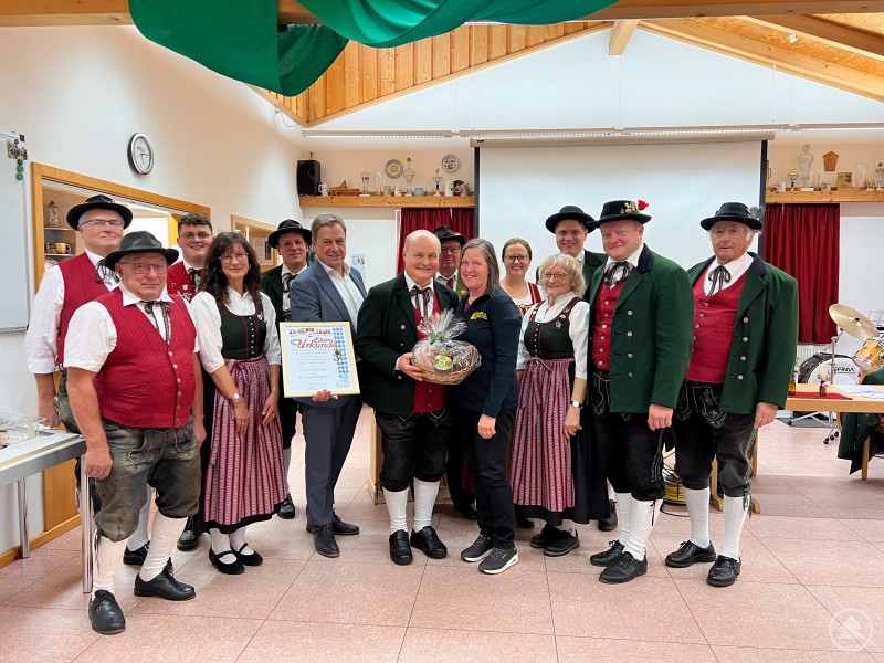 Gruppenfoto im Vereinsheim Haus i. Wald: Mitglieder des Musik- und Heimatvereins stehen in Tracht zusammen. In der Mitte h&auml;lt Franz Behringer eine Urkunde, daneben stehen Vereinsvertreter und Ehreng&auml;ste.