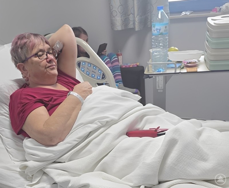 Manuela im Krankenhausbett in Antalya – erschöpft, aber stabil. Die Familie ist während der gesamten Behandlung an ihrer Seite. Manuela liegt in einem Krankenhausbett in Antalya, sichtbar geschwächt nach dem Schlaganfall. Neben ihr stehen Krankenhausutensilien, im Hintergrund sitzt ein Familienmitglied.