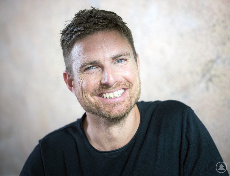 Autor und Schauspieler Leo Reisinger liest am 24. Oktober 2025 in der Kreisbibliothek Freyung aus seinem Roman „Bavarese“ Ein Mann mit Bart, Brille und Jacke sitzt vor einem Mikrofon und liest aus einem Buch.