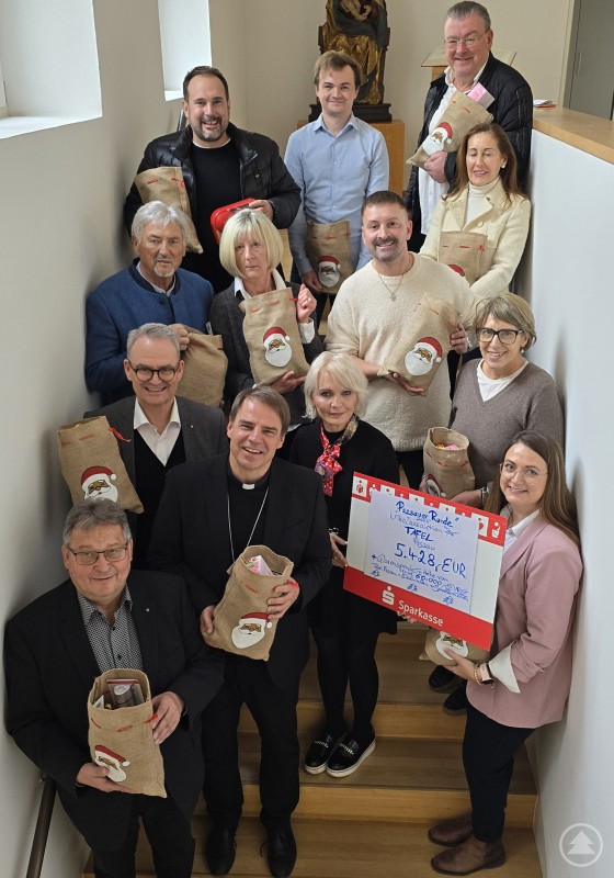 Gruppenfoto der Unterstützerinnen und Unterstützer der Nikolaus-Aktion mit den gepackten Sackerln. Eine große Gruppe von Spendern und Unterstützern steht gemeinsam auf einer Treppe und hält gefüllte Nikolaus-Sackerl sowie einen Spendenscheck.
