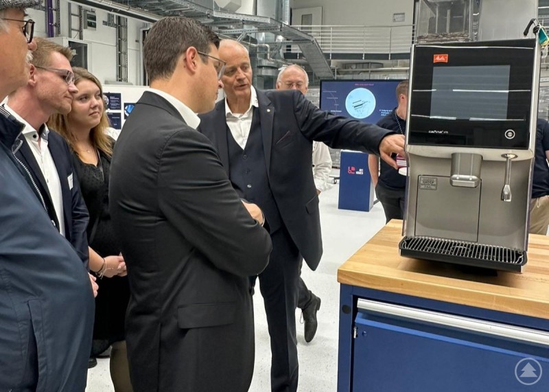 Ein Experte zeigt Besuchern eine moderne Anlage und erklärt deren Funktionen. Ein Mann erklärt einer Besuchergruppe eine moderne Maschine in einer Produktionshalle.