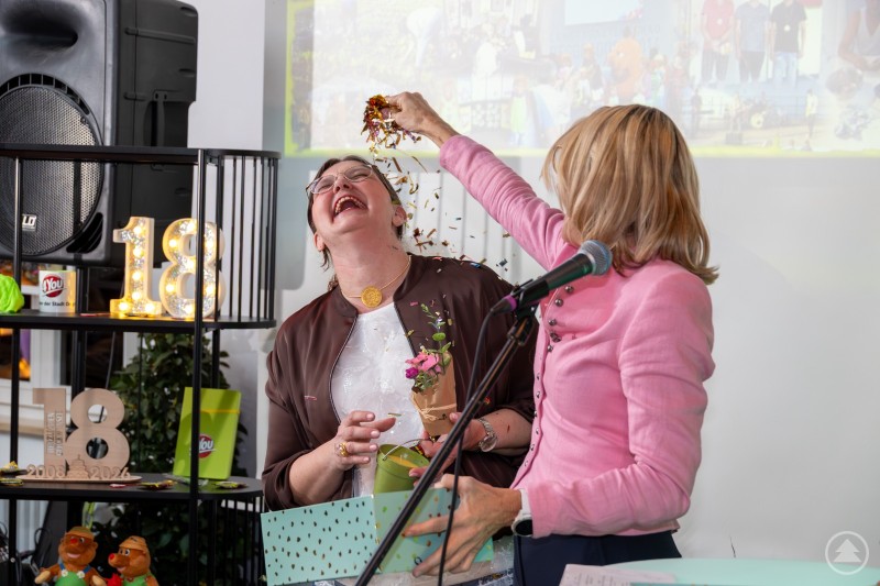 Renate Wasmeier und Karin Loibl beim Glitzer verteilen Renate Wasmeier verteilt bei der Jubiläumsfeier des Jugendcenters 4You Glitzer über Karin Loibl, die lachend reagiert.