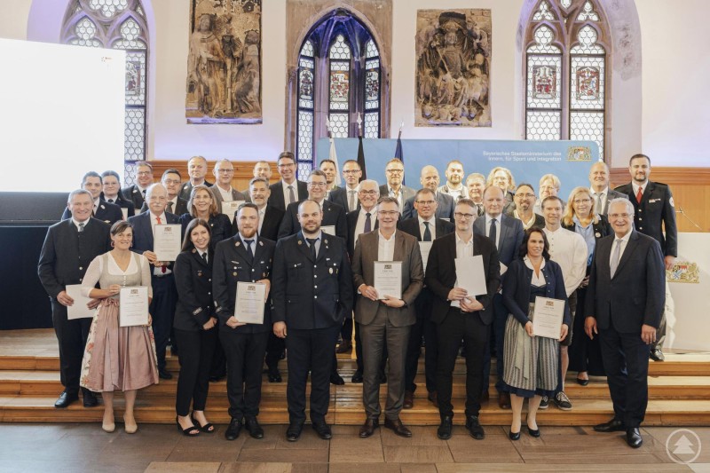 Eine große Gruppe von Feuerwehrangehörigen, Vertreterinnen und Vertretern aus Unternehmen sowie Politik posiert gemeinsam im historischen Rathaussaal in Nürnberg. Alle halten Urkunden in den Händen – im Hintergrund ist das Banner des Bayerischen Innenministeriums zu sehen.