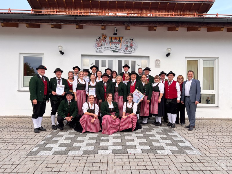 Die Ehrengäste mit einem Auszug der Geehrten im Verein. Gruppenfoto vor dem Vereinsheim in Haus i. Wald: Mitglieder des Musik- und Heimatvereins stehen in Tracht gemeinsam mit Ehrengästen vor dem Gebäude. Mehrere Geehrte halten Urkunden in den Händen, im Hintergrund ist das Vereinsheim zu sehen.