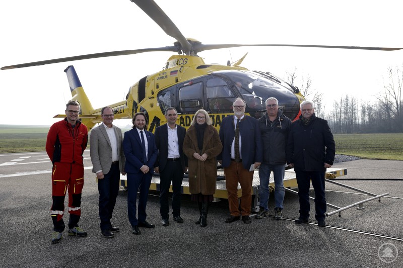 Bild v. l.: Flugretter Dr. Christoph Fiegl, Stützpunkteiter Cpt. Johannes Schöffl, ÖAMTC-Flugrettung Geschäftsführer Marco Trefanitz, Landrat Raimund Kneidinger, Landeshauptmann-Stellvertreterin Christine Haberlander, Oberbürgermeister Jürgen Dupper, Bürgermeister Gemeinde Suben Markus Wimmer und Vize-Bürgermeister Gemeinde Suben Werner Moser. Mehrere Personen stehen auf einem Hubschrauberlandeplatz vor einem gelben Rettungshubschrauber und posieren für ein Gruppenfoto.