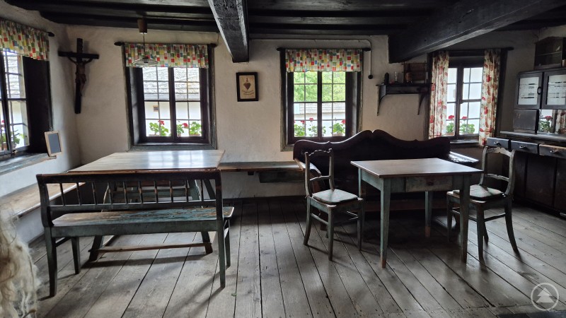 Stube im Petzi Hof Traditionell eingerichtete Bauernstube mit Holztischen und -bänken, Kachelöfen und Fenstern mit Gardinen.