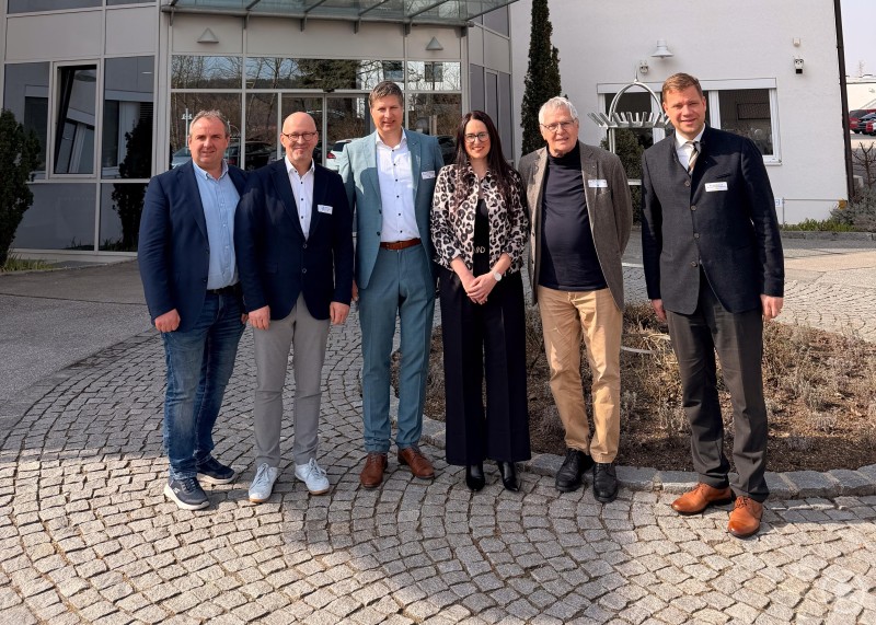 (von links nach rechts) Stefan Lang, Bürgermeister des Marktes Ortenburg; Kaspar Sammer, Geschäftsführer der Europaregion Donau-Moldau Niederbayern sowie der Euregio Freyung; Dr. Thomas Wisspeintner, Geschäftsführer der Micro-Epsilon Messtechnik GmbH & Co. KG; Jaroslava Pongratz, Netzwerkmanagerin Bayern-Böhmen; Karl Wisspeintner, ehem. Geschäftsführer der Micro-Epsilon Messtechnik GmbH & Co. KG; Dr. Olaf Heinrich, Bezirkstagspräsident von Niederbayern. Auf dem Foto stehen sechs Personen vor dem Firmengebäude von Micro-Epsilon in Ortenburg. Im Hintergrund ist der moderne Eingangsbereich mit Glasfassade und Firmenlogo zu sehen.